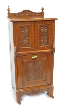 A late Victorian oak coal purdonium, the top with a carved raised back, above two carved panelled doors above a fall, above a carved apron, on castors, 108cm high, 52cm wide, 42cm deep.