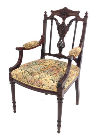 A late Victorian mahogany open armchair, with carved cresting rail and splat back, padded arms and over upholstered seat, in tapestry, on slender fluted legs.