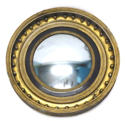 A Regency giltwood and gesso convex wall mirror, the moulded frame applied with spheres and with leaf border, surrounding an ebonised and reeded slip, 79cm diameter.