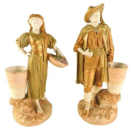 A pair of Royal Worcester porcelain blush ivory ground male and female figures, each standing beside a basket, the female with a basket of grapes, printed marks in puce to underside and pattern number 138, 25cm high.