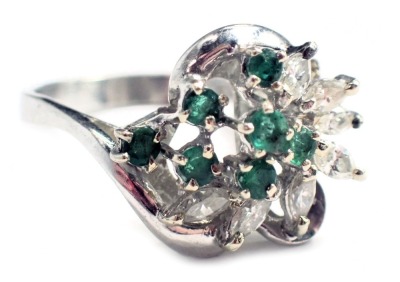 An emerald and diamond twist ring, set with seven round brilliant cut emeralds, each in four claw setting and surrounded by seven marquise cut diamonds, each in two claw setting of twist design, white metal stamped 18K, ring size O, 5.3g all in.