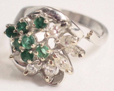 An emerald and diamond twist ring, set with seven round brilliant cut emeralds, each in four claw setting and surrounded by seven marquise cut diamonds, each in two claw setting of twist design, white metal stamped 18K, ring size O, 5.3g all in. - 2