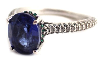 A dress ring, set with oval cut sapphire, surrounded by tiny emeralds to a raised shank setting with white metal set shoulders, stamped 0.50cts to band, white metal, marked 925, ring size R½, boxed. 