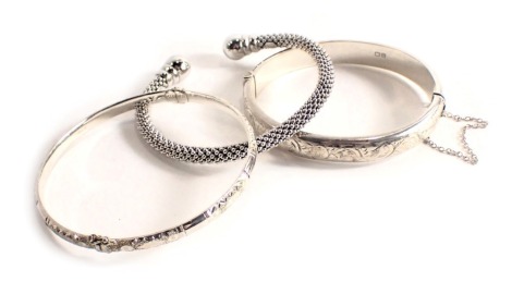 Three bangles, comprising a silver half hoop floral hinged bangle, a silver hammered design bangle, and a white metal torc bangle stamped 925, 42.1g all in. (3)