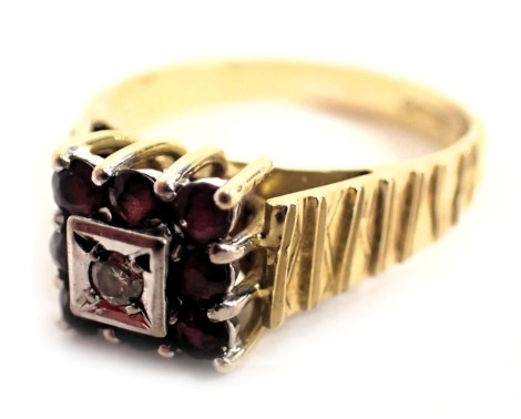 A 9ct gold dress ring, the square set panel with eight rubies, in claw setting with central tiny diamond in illusion platinum setting, on a bark effect band, ring size P, 4.8g all in.