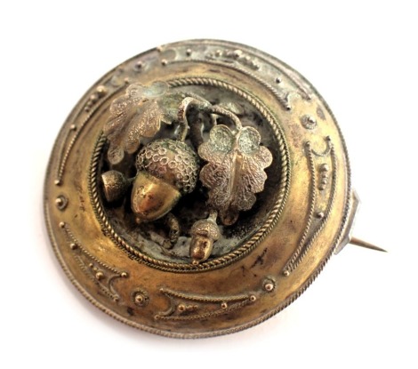 A Pinchbeck circular brooch, with raised filigree decoration and central acorn design, on single pin back, 2.5cm diameter.