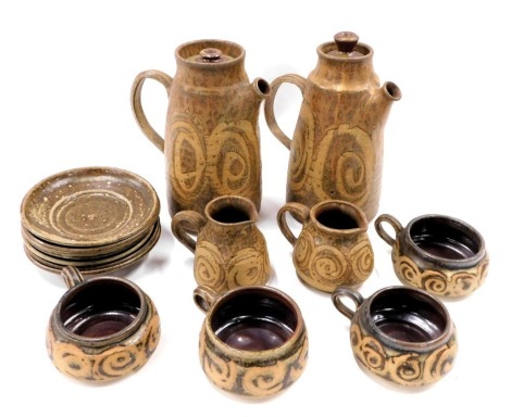 A studio pottery coffee set, on a brown ground with swirl glazed decoration to include two coffee pots, four cups and saucers, and two milk jugs.