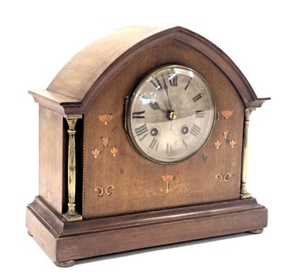 An Edwardian oak mantel clock, with arched top and boxwood tulip inlay and silvered dial, on columned supports with bun feet, thirty hour movement, 25cm high, 26cm wide. (AF)