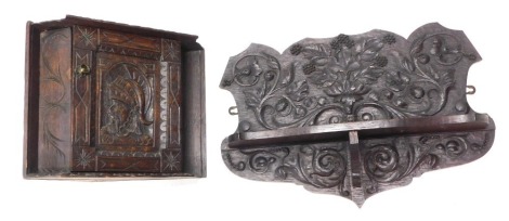 An oak wall shelf, carved with scrolls, berries, etc., 56cm wide, and a smaller carved oak corner cabinet, the door decorated with a Roman soldier, 39cm wide. (2)