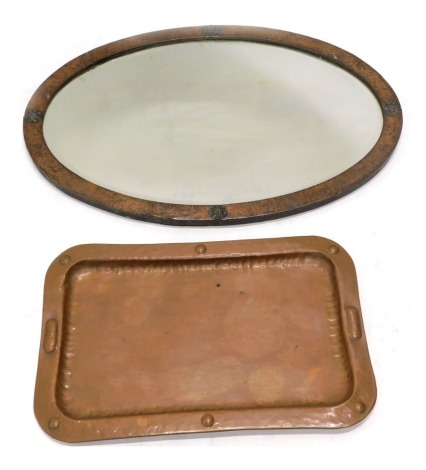 A late Arts and Crafts hammered copper oval wall mirror, with bevelled plate, decorated with roundels, 82cm wide, and an art nouveau rectangular hammered tray, unmarked, 59cm wide. (2)