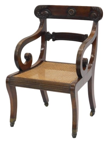 A Regency mahogany open armchair, the bar back carved with roundels and scrolls, with reeded shaped arms, the caned seat on sabre legs with castors.