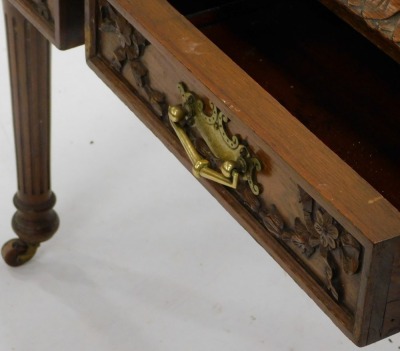 A late 19thC carved oak writing table, with a brown and gilt leather inset, and a leaf carved border, above two frieze drawers, on reeded turned tapering legs and brass and ceramic castors, 72cm high, 92cm wide. - 2