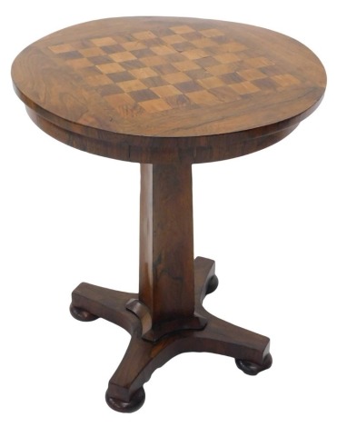 A William IV rosewood games table, the circular top inlaid with a chess board, hinged to reveal recesses for counters, gaming pieces, etc., on a concave tapering column and concave platform with bun feet, 68cm high, 56cm diameter.