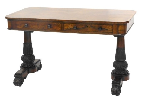 A William IV rosewood library table, the rectangular top with rounded corners, above two frieze drawers each with turned wood handles, on lappet and leaf carved end supports with scroll feet, 74cm high, 121cm wide, 68cm deep.