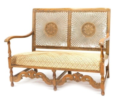 An early 20thC walnut bergere sofa, with a caned back, padded seat, shaped arms above a carved and pierced apron, on part turned legs, 115cm wide. (AF)