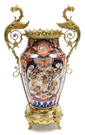 A Meiji period Imari porcelain and ormolu mounted vase, the coronet topped vase, with griffin handles, of shouldered, fluted form, painted with reserves of flowers on an iron red ground, raised on a pierced circular base, over four scroll feet, 49.5cm hig