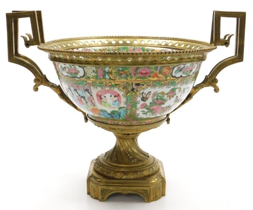 A 19thC Cantonese famille rose porcelain and ormolu mounted bowl, with a beaded and pierced mount and angular scroll handles, the bowl decorated with reserves of figures, and birds, butterflies and flowers, within a gilt ground decorated with fruit, flowe