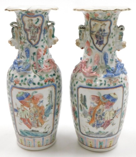 A pair of 19thC Cantonese famille rose porcelain vases, with a frilled neck and lion dog handles and moulded with dragons, having reserve panels of figures, within a floral ground, 25cm high. (AF)