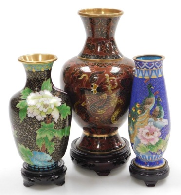 A Chinese red ground cloisonne vase, with stand, of baluster form, decorated with Imperial dragons chasing a flaming pearl, 20cm high, vase decorated with flowers on a black ground, 15.5cm high, and a vase decorated with peacocks on a blue ground, 15.5cm