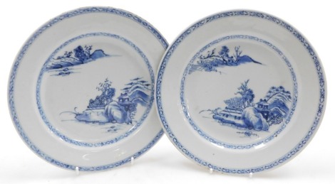 A pair of Qianlong porcelain blue and white plates, decorated with river landscapes, within hatched borders, 23.5cm wide.