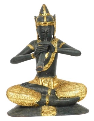 A Thai wooden and gilded carving of Prince Phra Aphai Mani, modelled seated playing his flute, with mirrored detailing, 70cm high.