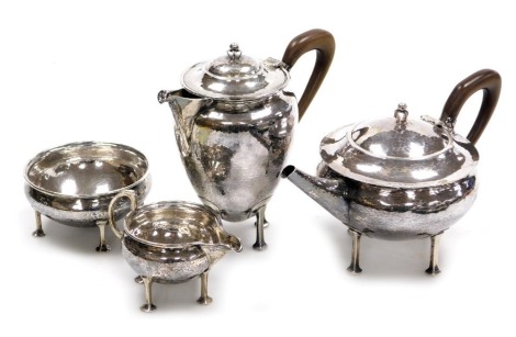 An Arts and Crafts silver four piece tea service, of compressed circular form, with lightly hammered decoration, raised on four square legs with pad feet, comprising teapot, hot water jug, cream jug and sugar bowl, A E Jones, Birmingham 1913, 1915, 1916, 