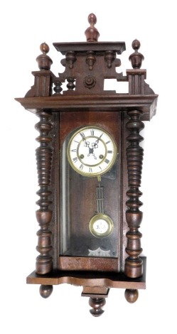 A late 19thC oak cased wall clock, the circular brass dial with enamel chapter ring bearing Roman numerals, eight day movement, the case with an urn top pediment, above a glazed door flanked by turned pilasters, with pendulum and key, 73cm high. (AF)