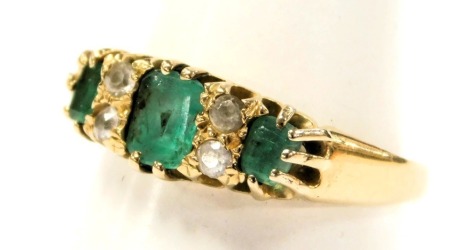 An 18ct gold and emerald three stone ring, interspersed with two pairs of diamonds at intervals, in a claw setting, size M, 2.6g.