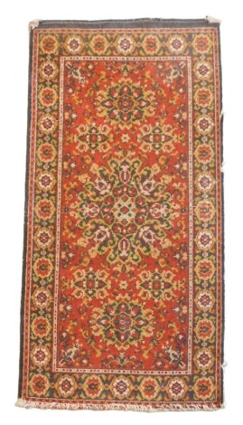 A Caucasian red ground rug, decorated with a large central medallion, two smaller medallions and four flowers, within a repeating floral border, 129cm x 65cm.