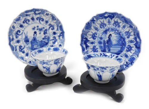 A pair of Kangxi porcelain blue and white tea bowls and saucers, of moulded floral form, decorated with figures beneath blossom and dragons, internally with a four claw dragon and panels of flowers, with stands.