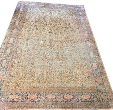 A Kashan silk cream ground rug, the central rectangular field decorated with flowers and scrolling leaves, within repeating floral and foliate borders, the widest border also with reserves of Arabic script, 420cm x 306cm.