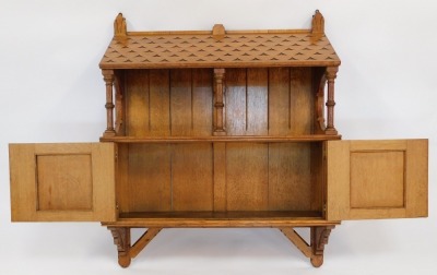 A late 19thC Gothic Revival oak hanging cupboard, the drawer stamped L W Collmann 2572, of architectural form, with sloping 'roof canopy' above an open shelf, with three turned column supports, the cupboard below enclosed by two doors with marquetry inlay - 2