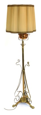 An Art Nouveau brass standard lamp, formerly an oil lamp later converted, with copper central reservoir on a cylindrical column, with scroll work adornments raised on four shell capped feet, with shade, 168cm high overall.