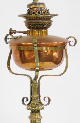 An Art Nouveau brass standard lamp, formerly an oil lamp later converted, with copper central reservoir on a cylindrical column, with scroll work adornments raised on four shell capped feet, with shade, 168cm high overall. - 2