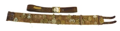 A canvas and leather belt containing various cap badges, to include Hampshire Regiment, Prince Albert's Own South Africa 1900-2, York and Lancaster Regiment, Dorsetshire Regiment, etc. together with a leather belt with buckle.