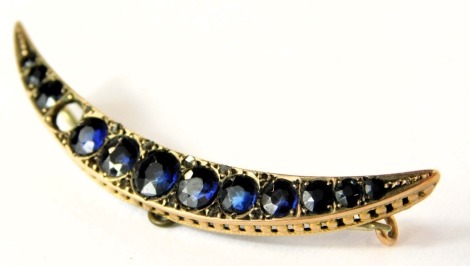 A 9ct gold sapphire crescent moon brooch, set with graduated design sapphires, with pierced outer border, the largest stone 4.8 x 4.2 x 2.2, the smallest stone 1.8 x 1.8 x 1.2, one stone missing, in yellow metal frame on single pin steel back, 5cm wide.