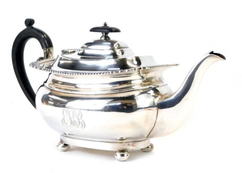 A George V silver teapot, with shell capped reeded borders, with an ebonised knop and handle, on bun feet bearing the crest EKB, maker Harrison Brothers & Howson, London 1911, 23.24oz all in.