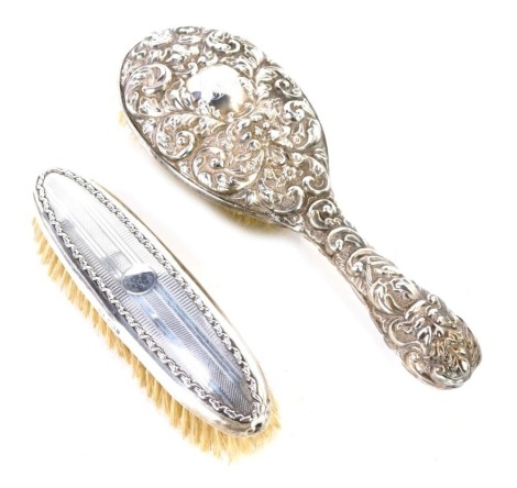 Two silver backed dressing table brushes, comprising a hand brush with heavy floral and bird scroll decoration, bearing the initials EKB, Walker and Hall, Chester 1907, and a silver backed clothes brush, Birmingham 1912. (2)