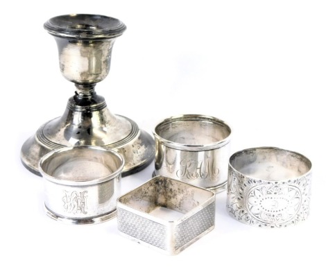 A group of silver wares, comprising four silver napkin rings, all George V and later, of varying decoration, 2.94oz, and a silver squat candlestick with loaded base. (5)