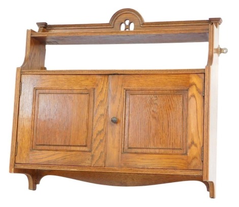 An Edwardian oak smoker's cabinet, with an arched and pierced top above two shelves with two cupboard doors, 51cm high, 58cm wide, 19cm deep.