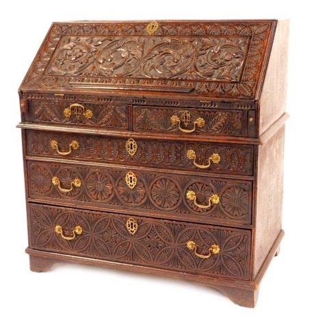 An 18thC oak bureau, with later heavily carved foliate scrolls and flower heads, with fall flap opening to reveal arrangement of drawers and cupboard, above two short and three long drawers with brass swing handles, on bracket feet, 105cm high, 91cm wide,