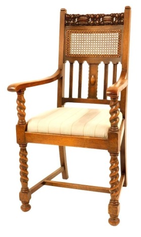 An early 20thC oak open armchair, with a part woven cane panelled back and carved floral top rail, with a later upholstered drop-in seat, 112cm high.