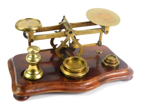 A set of vintage brass postal scales, with weights, raised on a serpentine base, 19cm wide.