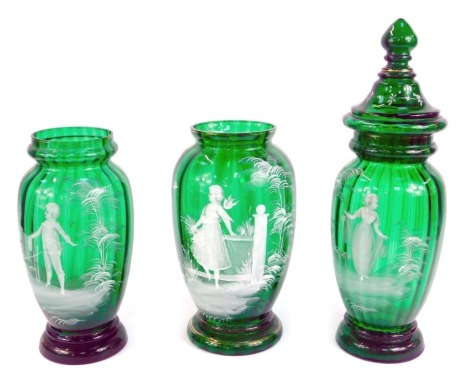 A pair of Mary Gregory style green glass jars, one with a cover, decorated with a boy and girl in a garden, 43cm and 29cm high respectively, and a further Mary Gregory style green glass vase, similarly decorated with a girl in a garden, 29cm high. (3)