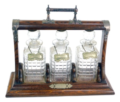 A late 19thC oak and plate mounted Tantalus, with three cut glass decanters and stoppers, each with plated decanter labels, with key.