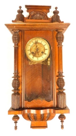 A late 19thC American walnut and oak cased wall clock, circular brass dial with enamel chapter ring bearing Roman numerals, eight day movement with coil strike, the case with an urn topped pediment, over an arched door flanked by turned pilasters, with pe