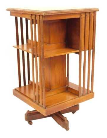 An Edwardian Sheraton Revival inlaid mahogany revolving book stand, of square section design, with numerous shelves and fitted with three shallow drawers, on a quadruped base with pot castors, 86cm high, 47cm x 47cm square.