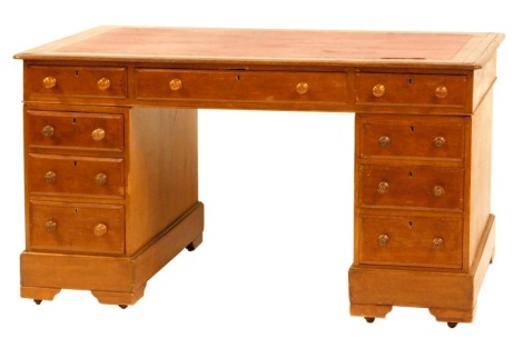 An early 20thC oak kneehole desk, with inset red leather top and fitted with a three drawers to the frieze and three graduated drawers to each pedestal, with turned knop handles and on castors, 76cm high, 136cm wide, 78cm deep.