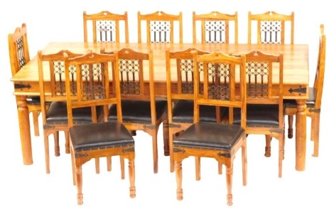 An Indonesian hardwood rectangular dining table, with plain plank top and frieze, on plain cylindrical turned legs, 76cm high, 240cm x 121cm, and a set of twelve chairs, with ironwork backs and over upholstered seats in black leatherette, with iron strap 