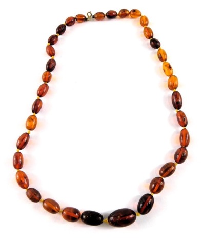 A Baltic amber graduated beaded necklace, the oblong beads on a knotted string strand, the largest 2cm wide, the smallest 8mm wide, with a yellow metal clasp, unmarked believed to be 9ct gold, 48cm long, 19.5g all in.